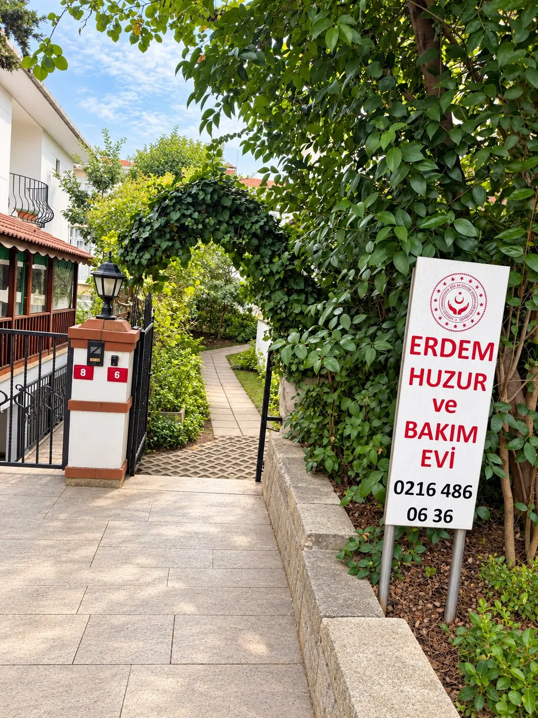 Erdem Huzur ve Bakım Evi tabelası, sarmaşıkla kaplı kemerli bahçe girişi ve fenerli kapı