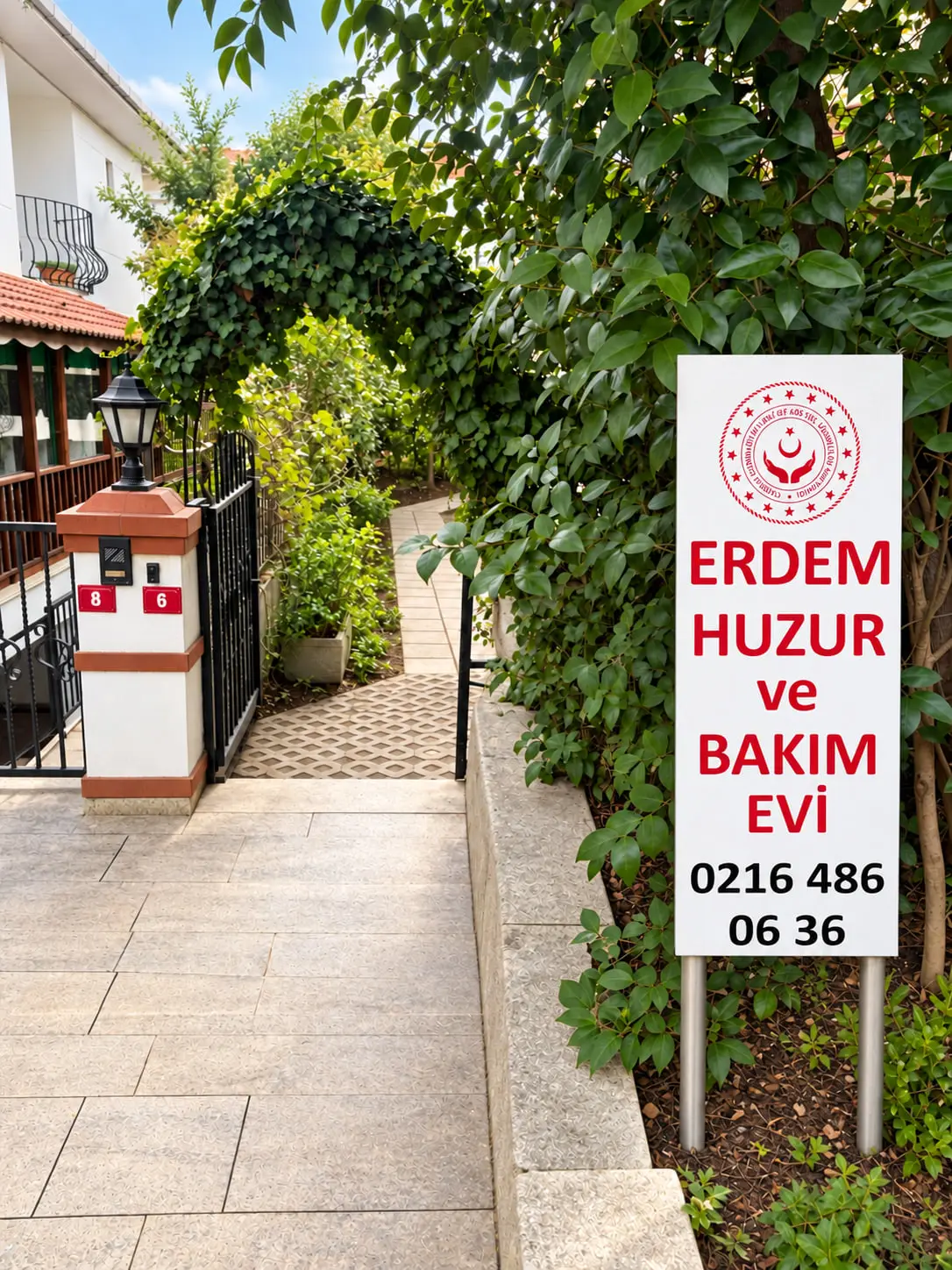 Erdem Huzur ve Bakım Evi tabelası, sarmaşıkla kaplı kemerli bahçe girişi ve fenerli kapı