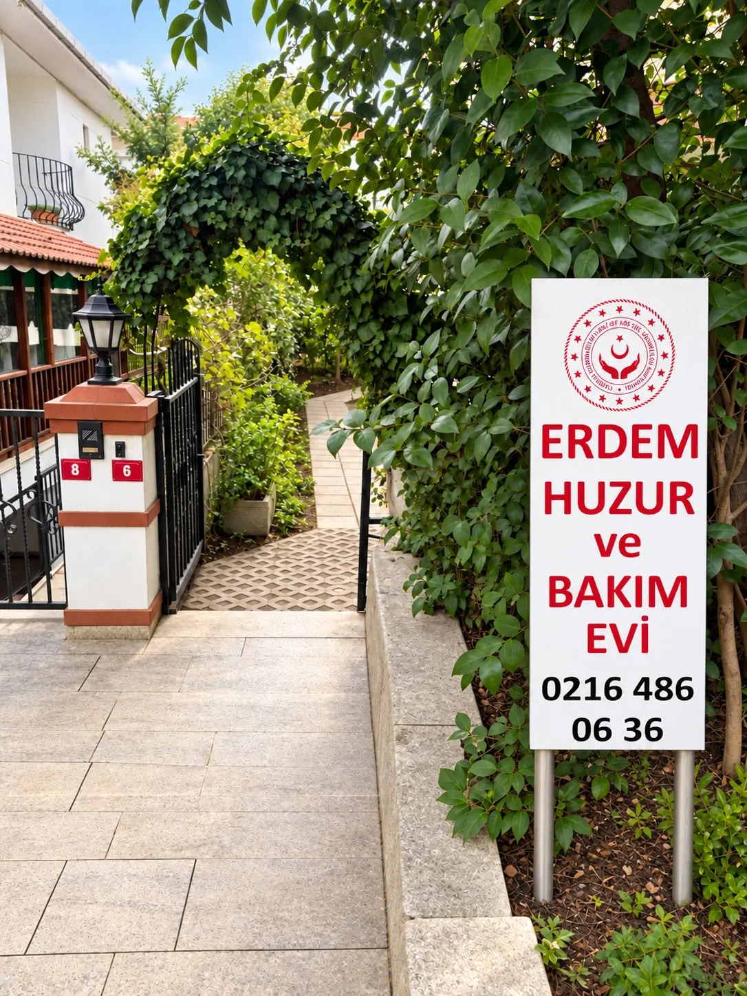 Erdem Huzur ve Bakım Evi tabelası, sarmaşıkla kaplı kemerli bahçe girişi ve fenerli kapı